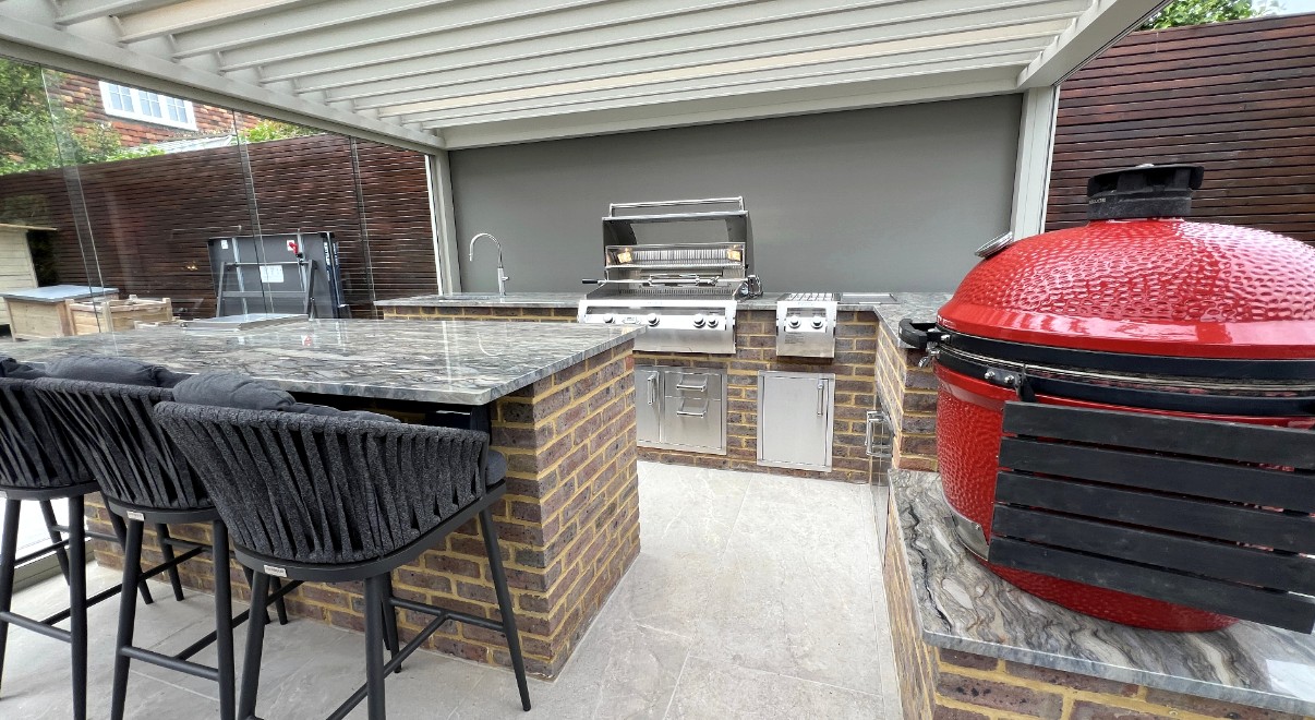 Outdoor kitchen with a marble island and grill beneath a white louvred pergola roof